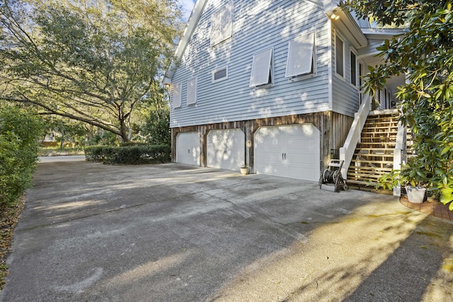 view of side of property with an attached garage, concrete driveway, and stairway