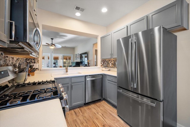 kitchen with appliances with stainless steel finishes, sink, gray cabinetry, ceiling fan, and light hardwood / wood-style floors