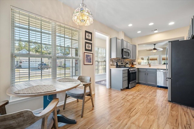 kitchen with tasteful backsplash, hanging light fixtures, gray cabinets, stainless steel appliances, and light hardwood / wood-style floors