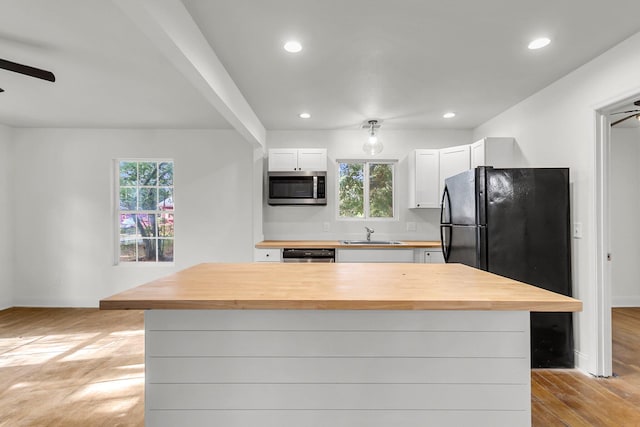 kitchen featuring white cabinets, appliances with stainless steel finishes, a center island, butcher block counters, and sink