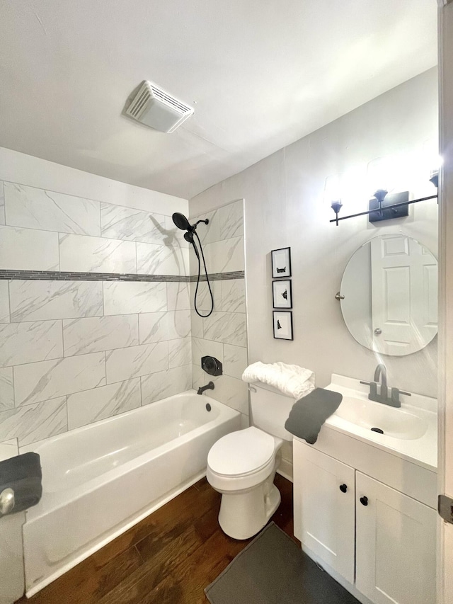 full bathroom featuring hardwood / wood-style floors, tiled shower / bath combo, vanity, and toilet