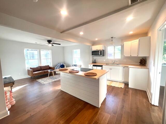 kitchen featuring white cabinetry, stainless steel appliances, dark hardwood / wood-style flooring, a kitchen island, and beamed ceiling