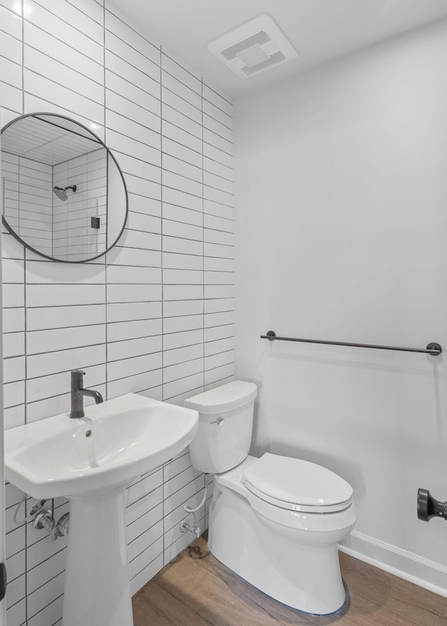 bathroom featuring wood-type flooring, toilet, and tile walls