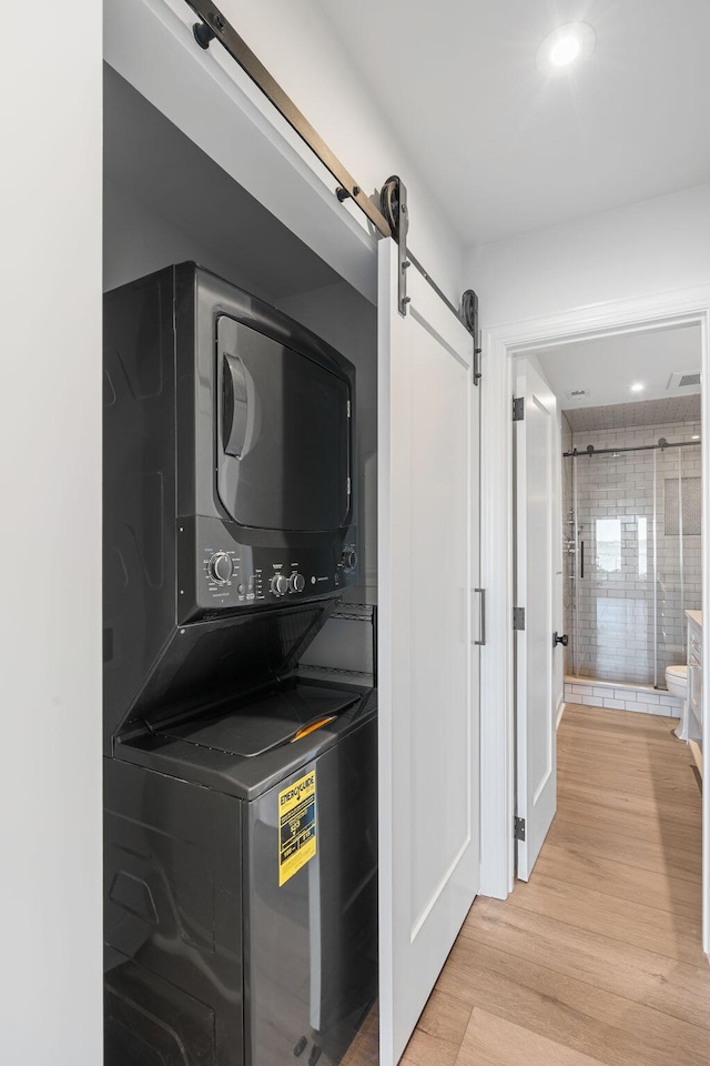 laundry room with stacked washer / drying machine, a barn door, and light wood-type flooring