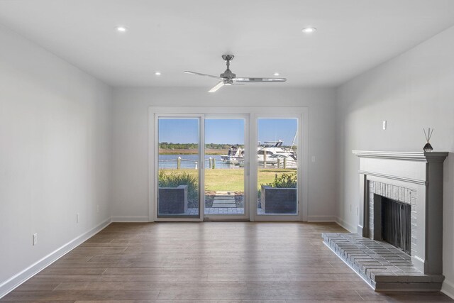 unfurnished living room featuring a water view, ceiling fan, dark hardwood / wood-style flooring, and a brick fireplace