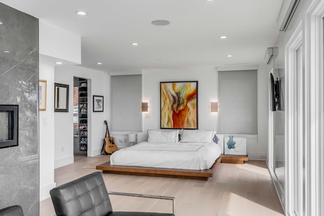 bedroom with a high end fireplace and light hardwood / wood-style floors