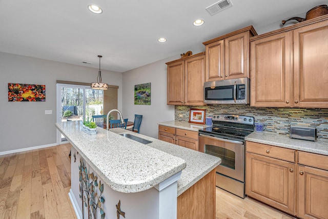 kitchen featuring sink, stainless steel appliances, tasteful backsplash, pendant lighting, and a kitchen island with sink