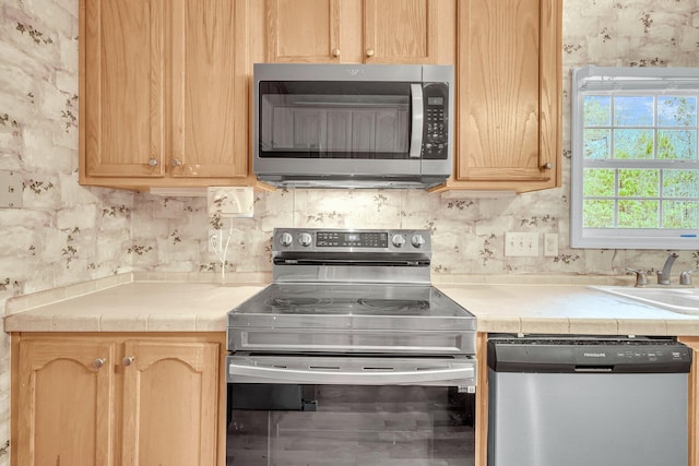 kitchen featuring appliances with stainless steel finishes, sink, decorative backsplash, tile counters, and light brown cabinets