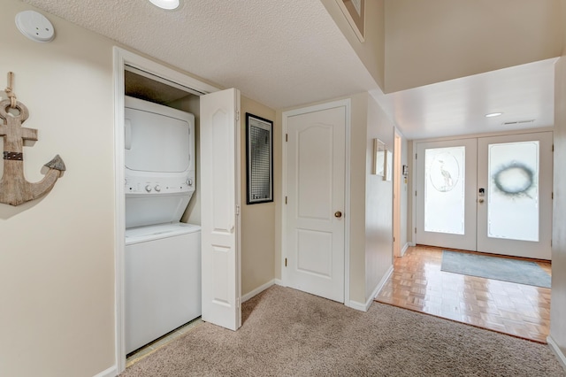 entryway with stacked washer and dryer, a textured ceiling, french doors, carpet floors, and baseboards