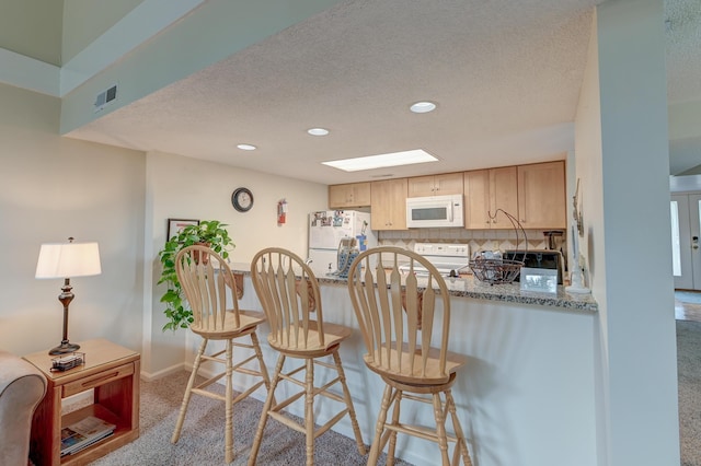 kitchen featuring white appliances, visible vents, a textured ceiling, a kitchen bar, and backsplash