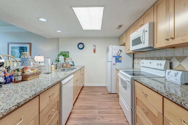 kitchen with tasteful backsplash, light wood finished floors, light stone countertops, white appliances, and a sink