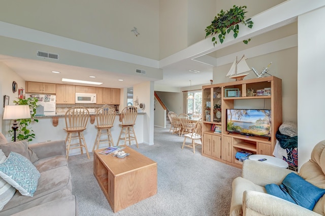 living area with light carpet, visible vents, recessed lighting, and a towering ceiling