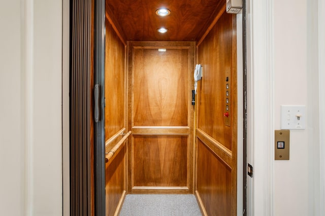 interior details with carpet floors, wooden walls, and elevator