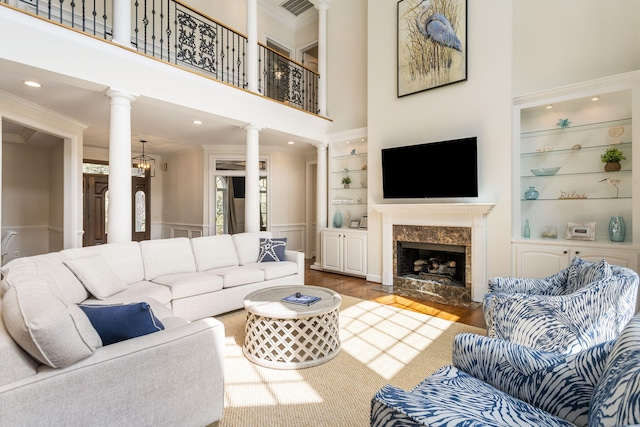 living room with a high end fireplace, hardwood / wood-style flooring, built in shelves, a towering ceiling, and ornate columns