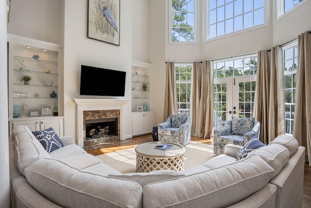 living room featuring built in shelves, a high end fireplace, french doors, hardwood / wood-style flooring, and a towering ceiling