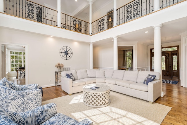 living room featuring a high ceiling, decorative columns, hardwood / wood-style floors, and crown molding