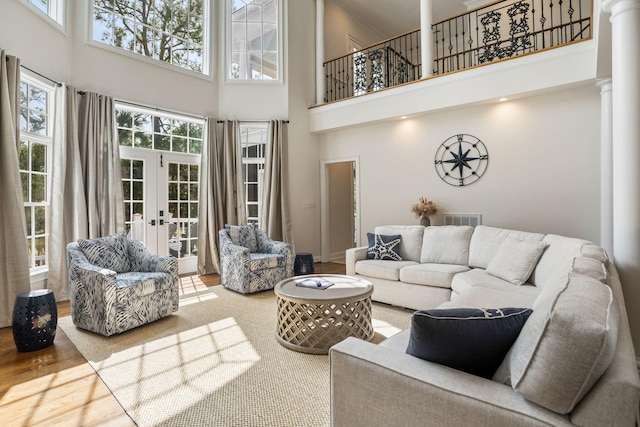 living room featuring french doors, hardwood / wood-style flooring, decorative columns, and a high ceiling