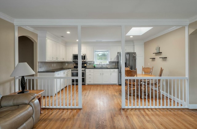 kitchen with light wood-type flooring, stainless steel appliances, white cabinetry, and backsplash