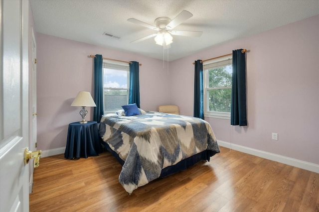 bedroom featuring a textured ceiling, ceiling fan, light hardwood / wood-style flooring, and multiple windows