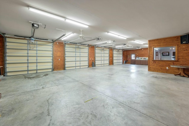 garage featuring ceiling fan, a garage door opener, and wooden walls