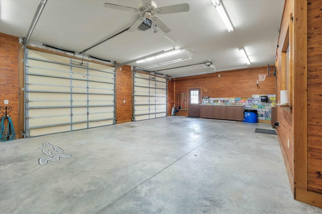 garage featuring ceiling fan, wooden walls, and a garage door opener