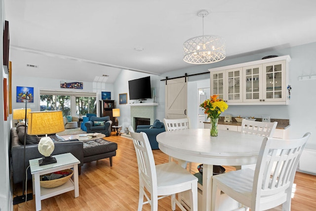 dining space with a brick fireplace, a chandelier, light wood-type flooring, and a barn door