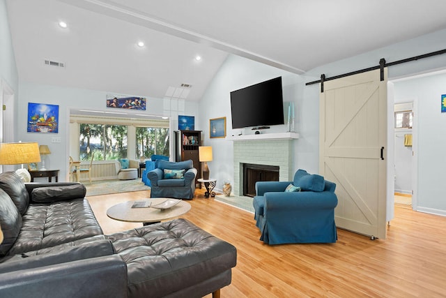 living room with lofted ceiling, a barn door, wood-type flooring, and a fireplace