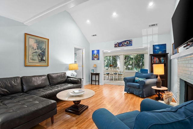 living room with light hardwood / wood-style floors, high vaulted ceiling, and a brick fireplace