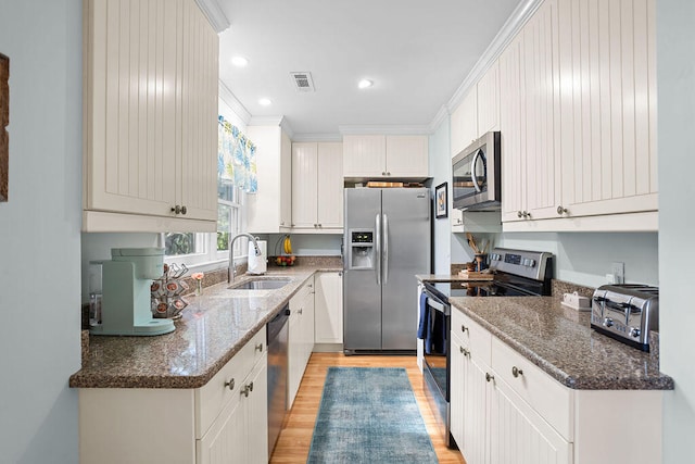 kitchen with light hardwood / wood-style flooring, stainless steel appliances, dark stone countertops, sink, and white cabinets