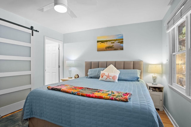 bedroom featuring hardwood / wood-style floors, a barn door, and ceiling fan