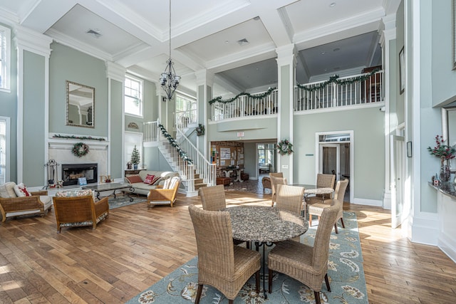 dining area featuring hardwood / wood-style flooring, a premium fireplace, plenty of natural light, a high ceiling, and coffered ceiling