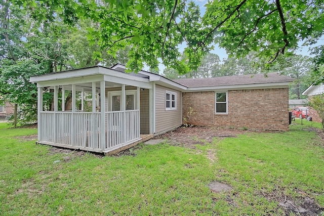 back of property with a sunroom, brick siding, and a yard