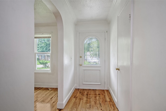 entryway featuring arched walkways, crown molding, light wood finished floors, a textured ceiling, and baseboards