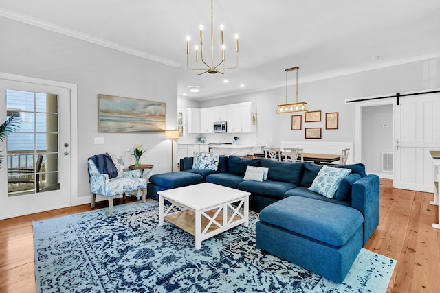 living room featuring an inviting chandelier, crown molding, light hardwood / wood-style flooring, and a barn door