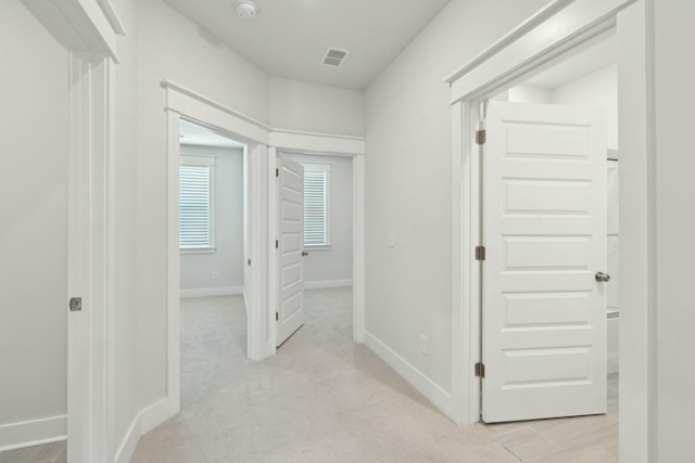 corridor featuring light carpet, baseboards, and visible vents