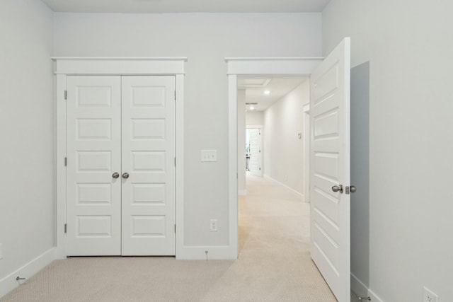 unfurnished bedroom with light carpet, a closet, and baseboards