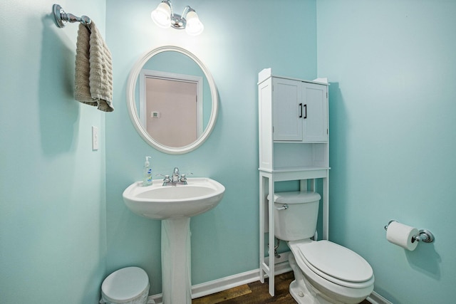 half bathroom featuring wood finished floors, toilet, baseboards, and a sink