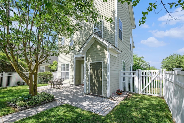 rear view of property featuring a fenced backyard, a gate, a patio, and a lawn