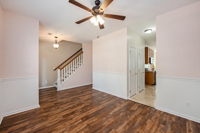 unfurnished room with a ceiling fan, stairs, wood finished floors, baseboards, and visible vents