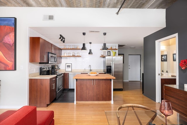 kitchen with appliances with stainless steel finishes, wood counters, decorative backsplash, light hardwood / wood-style floors, and hanging light fixtures