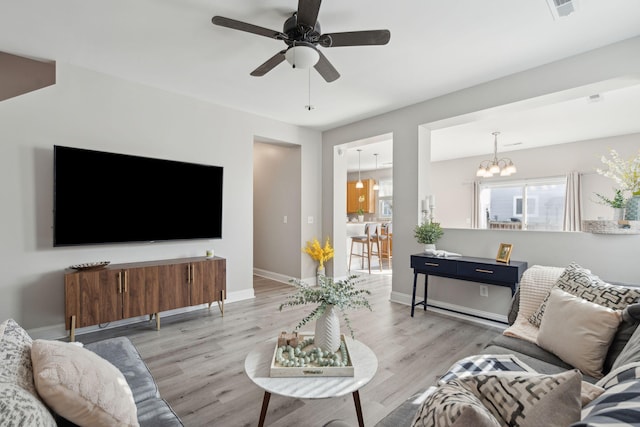 living area featuring baseboards, visible vents, wood finished floors, and ceiling fan with notable chandelier