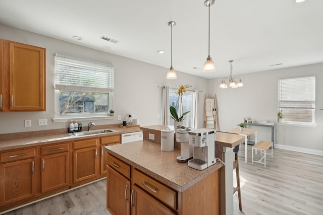 kitchen featuring white dishwasher, light wood-style flooring, a kitchen island, a sink, and brown cabinets