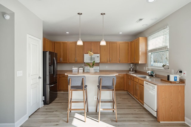 kitchen with white appliances, a kitchen island, a sink, light wood-style floors, and light countertops