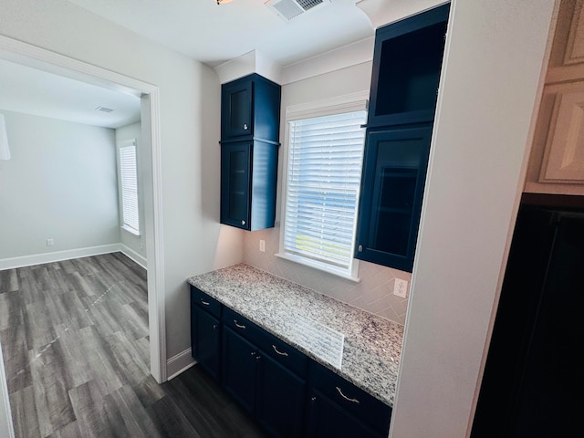 kitchen with blue cabinetry, hardwood / wood-style flooring, light stone countertops, and tasteful backsplash