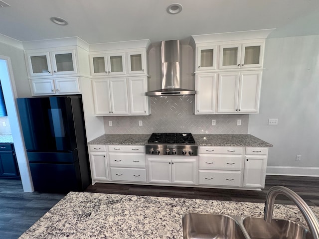 kitchen with stainless steel gas stovetop, wall chimney range hood, light stone counters, and black fridge