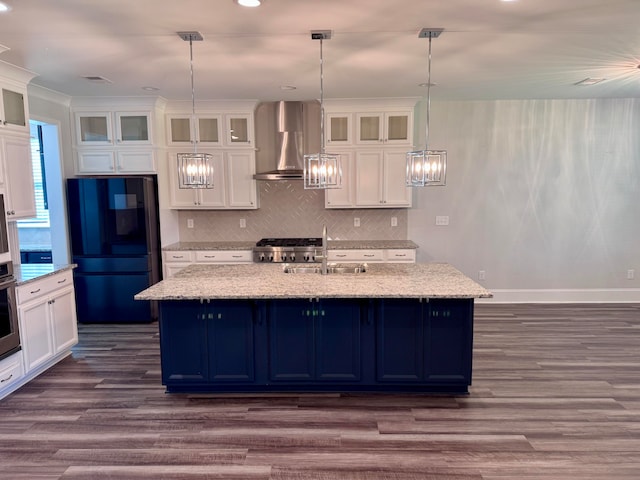 kitchen featuring wall chimney range hood, an island with sink, appliances with stainless steel finishes, and dark hardwood / wood-style floors