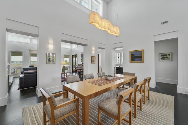 dining room with a high ceiling, visible vents, a wealth of natural light, and dark wood-type flooring
