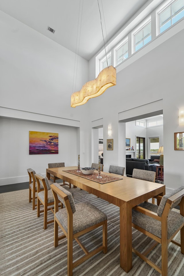dining room featuring baseboards, visible vents, a healthy amount of sunlight, and a towering ceiling