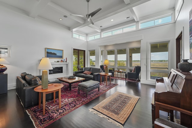 living area with a towering ceiling, ceiling fan, beam ceiling, and coffered ceiling