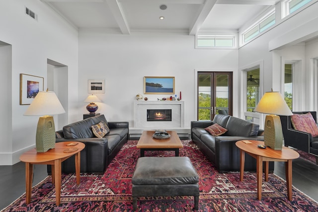 living area with a lit fireplace, beamed ceiling, visible vents, and a towering ceiling